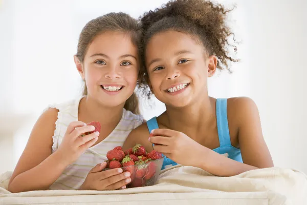 Две молодые девушки, ест клубнику в гостиной улыбается — стоковое фото