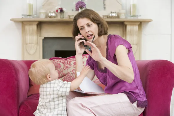 Мать, используя телефон в гостиной с ребенком хмурится — стоковое фото