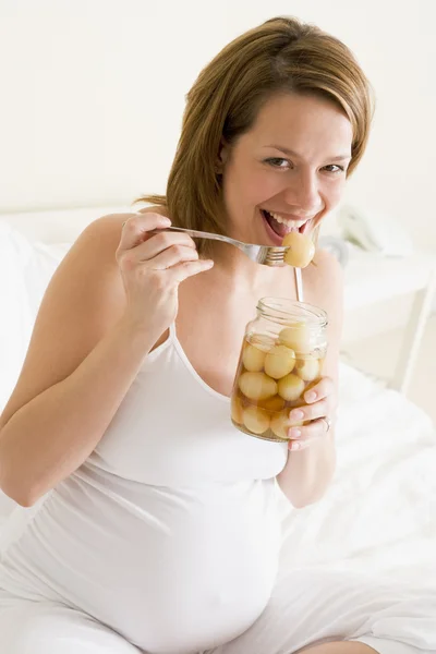 Беременная женщина в постели, едят соленые яйца улыбается — стоковое фото