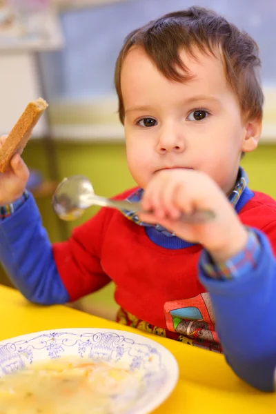 Маленький мальчик ест в детском саду — стоковое фото
