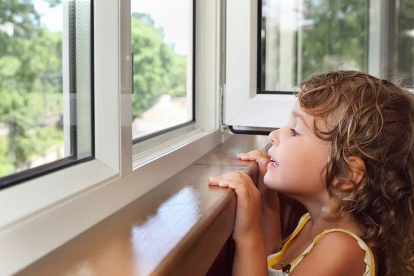 Довольно улыбается маленькая девочка на балконе, взгляд из окна — стоковое фото