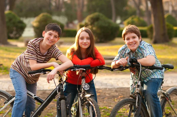 Два улыбаясь подростков мальчиков и одна девочка-подросток, весело на велосипедах в парке — стоковое фото