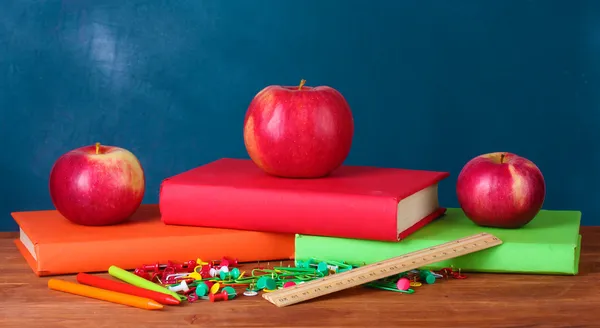 Состав книг, канцелярских принадлежностей и яблоки на столе учителя на фоне доски — стоковое фото