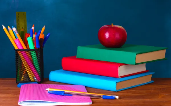 Состав книг, канцелярских принадлежностей и яблоко на столе учителя на фоне доски — стоковое фото