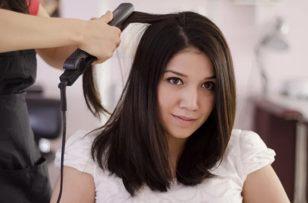 Женщина-парикмахер выпрямляет волосы — стоковое фото